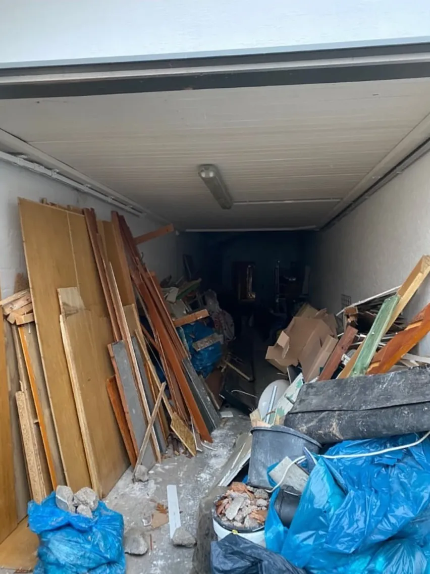 Garage mit Holzplatten, Bauschutt und blauen Säcken vor der Entrümpelung
