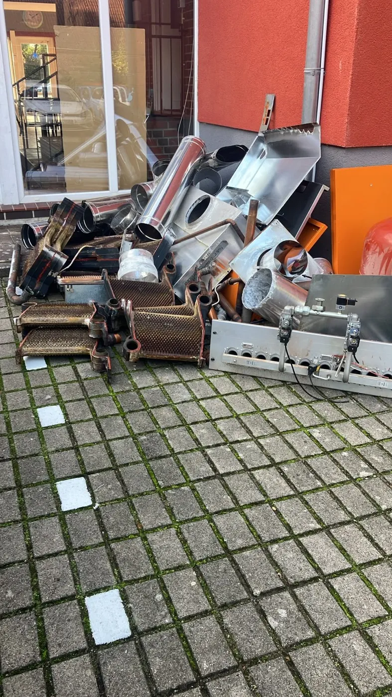 Haufen aus Heizungsteilen, Edelstahlrohren und Kupfer vor einem Gebäude